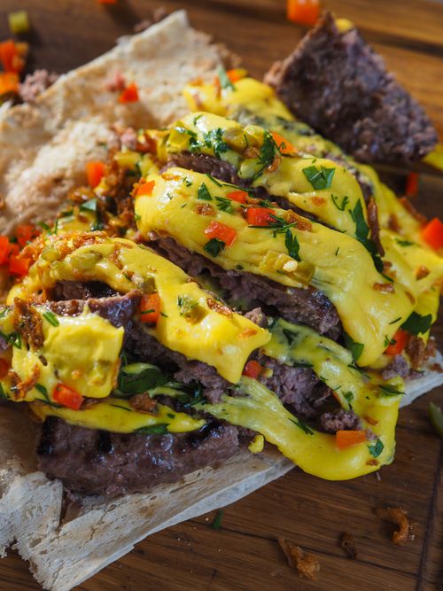 Free Close-up of a savory beef sandwich topped with melty cheese and vibrant garnishes. Stock Photo