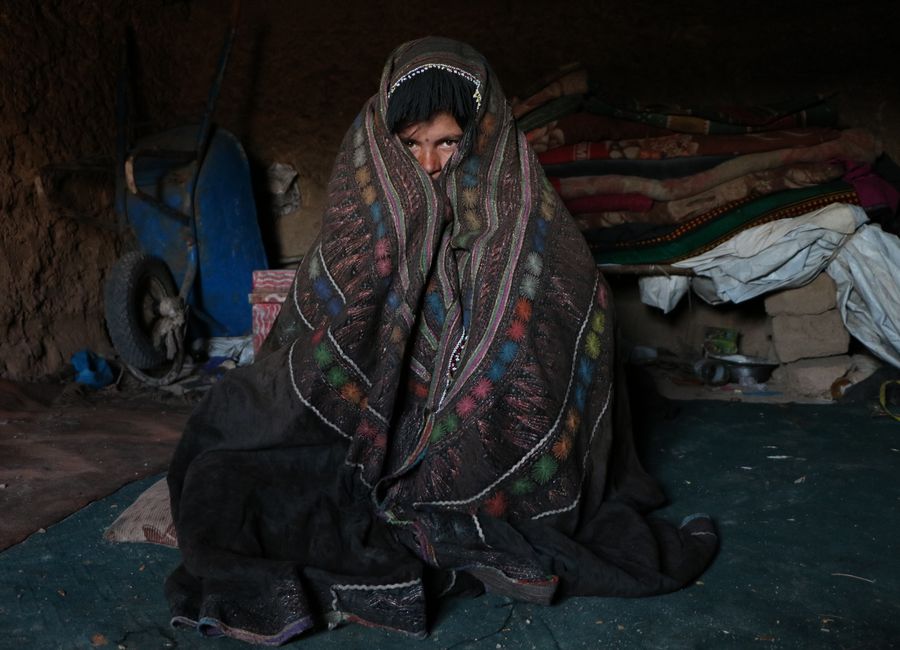 A person wrapped in a colorful blanket sitting in a dimly lit indoor space in Herat, Afghanistan.