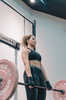 A young woman powerlifting heavy weights indoors, showcasing strength and fitness.