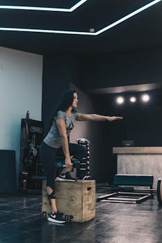 A young woman performing a fitness routine indoors at a gym, stepping on a box.