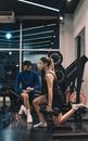 Young Woman Kneeling with Exercise Dumbbell in Hand and Man Accompanying Her