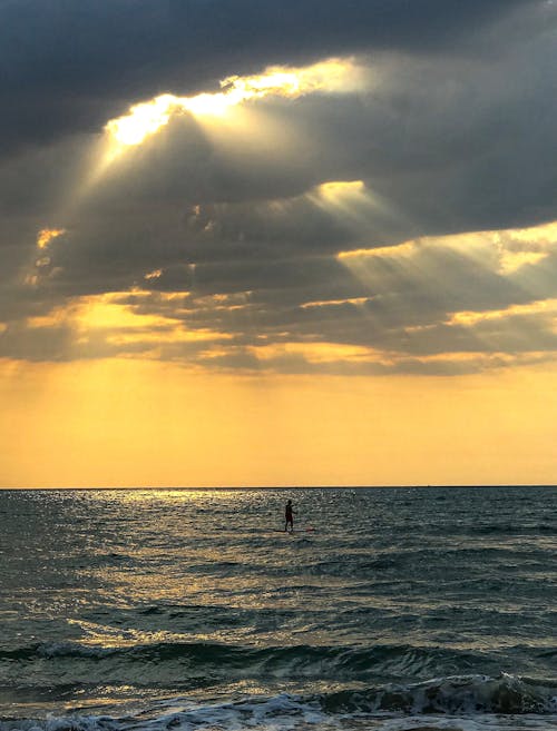 A Person in Body of Water Under the Cloudy Sky with Ray of Lights