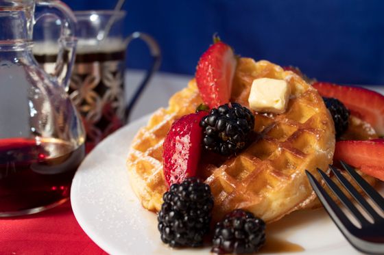 Golden Belgian waffle with a pat of butter, strawberries, blackberries and maple syrup