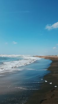A serene beach scene with gentle waves lapping against the shore under a clear blue sky.