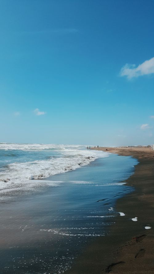 Free A serene beach scene with gentle waves lapping against the shore under a clear blue sky. Stock Photo