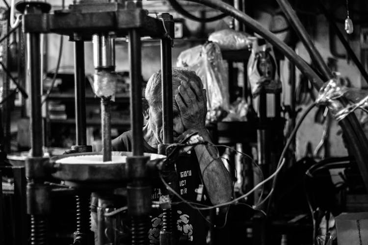 Man With Hand On Face Near A Machinery In A Factory