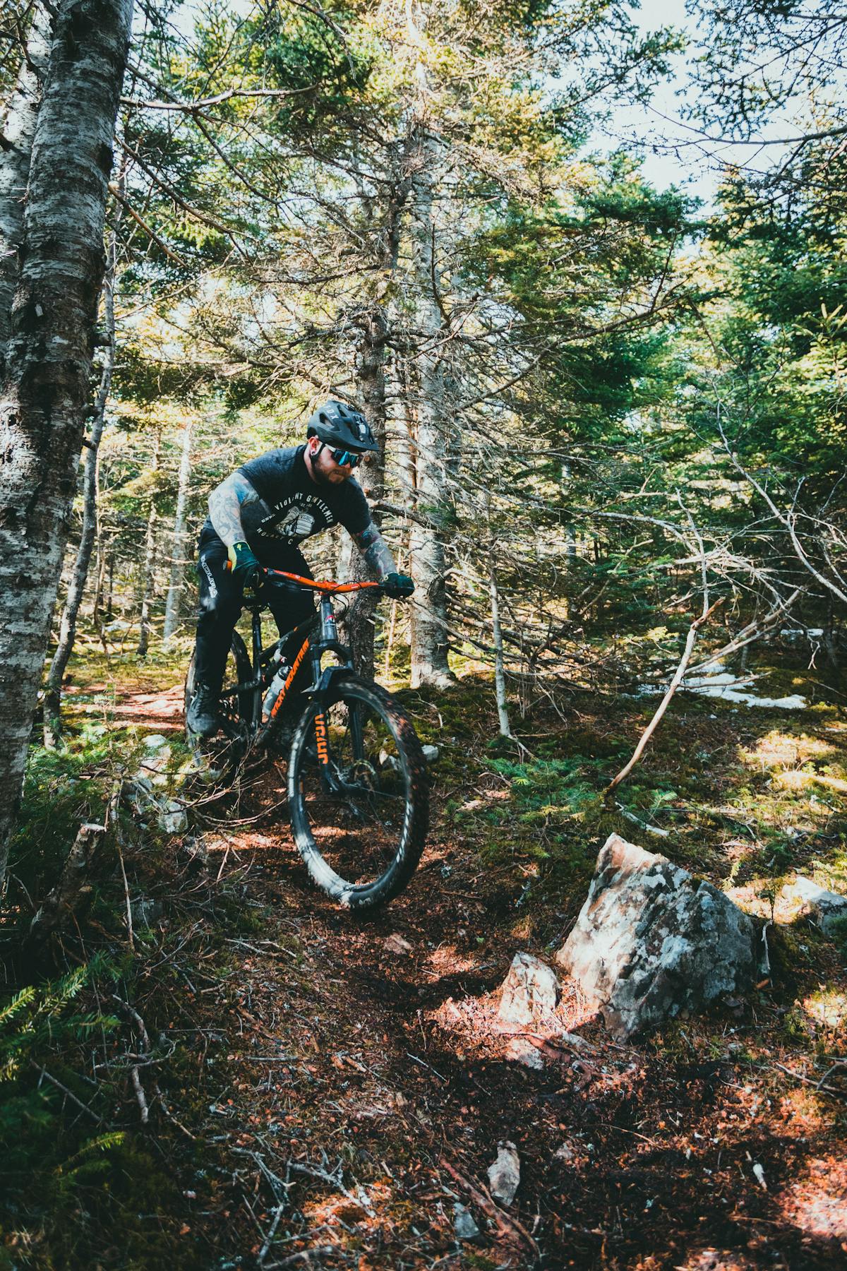 Mountain biker riding through dense forest trail with full suspension bike handling roots and rough terrain
