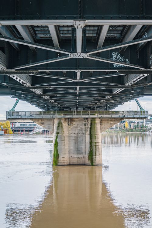 Free A steel bridge spanning a river with a concrete foundation and reflections. Stock Photo