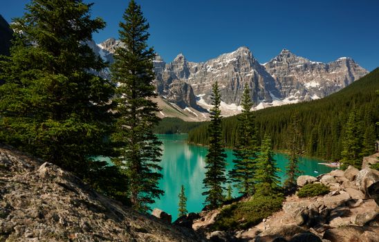 Stunning turquoise waters of Moraine Lake surrounded by rocky mountains and lush pine trees in Banff National Park.