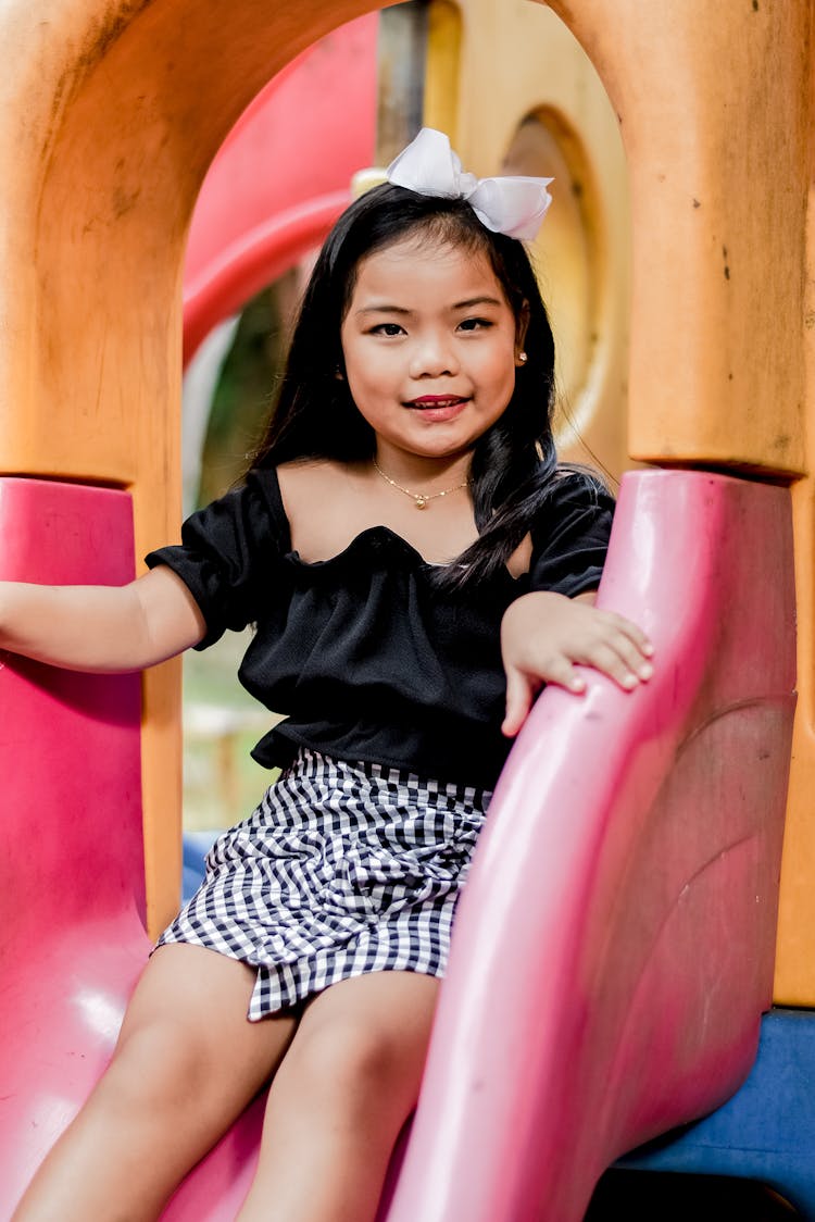 Cute Girl In Black Top And Checkered Skirt In A Slide 