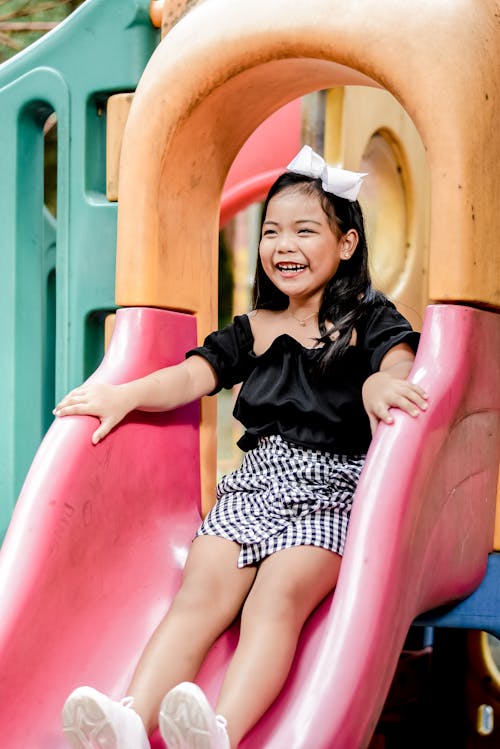 Free happy Little Girl Sitting on Plastic Slide in the Park Stock Photo