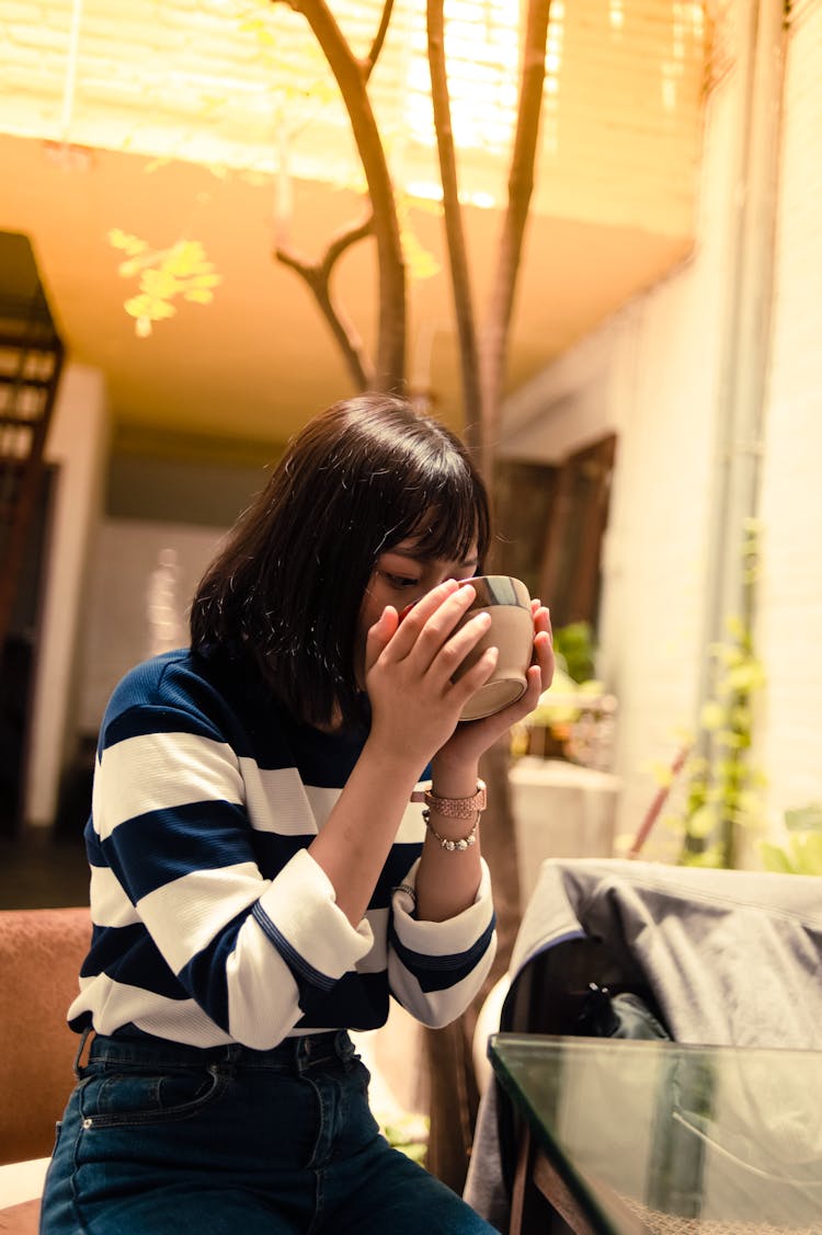 Woman Seated Outside Drinking From A Brown Bowl