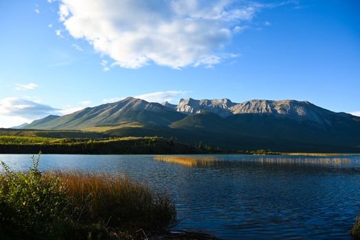 A tranquil lake with mountains in Jasper, Alberta, under a bright blue sky.