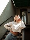Woman in White Long Sleeve Shirt and Blue Denim Daisy Dukes Standing Beside Gray Concrete Wall