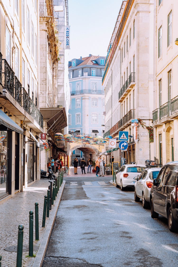 A Street With People And Parked Cars Near Buildings