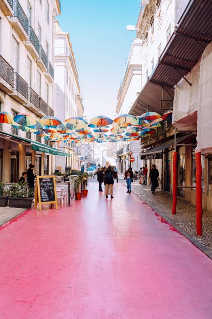Charming Lisboa street scene featuring a pink pavement and colorful umbrellas suspended above, creating a lively atmosphere.