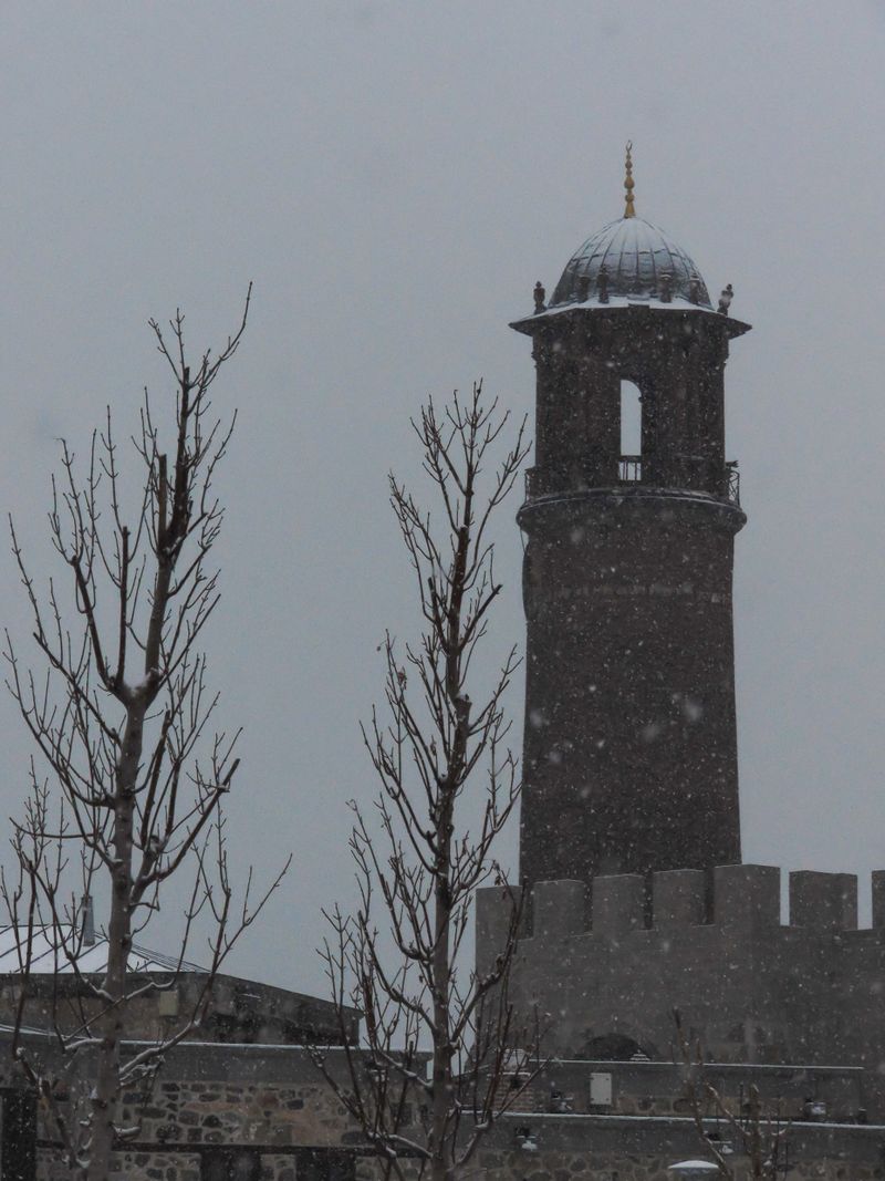 A captivating view of Erzurum Castle under a serene snowfall, showcasing its historic tower and walls.