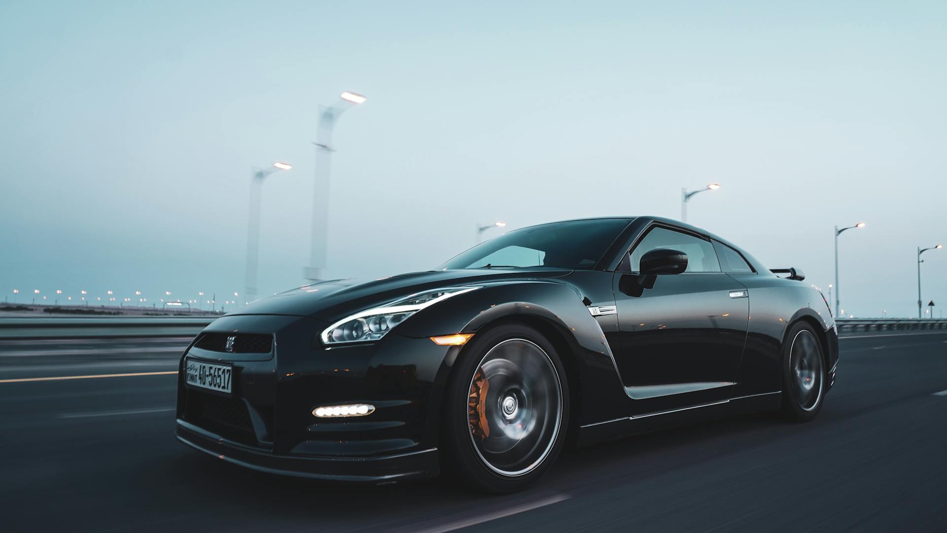 Dynamic black sports car driving on a highway in Kuwait at dusk, showcasing speed and elegance.