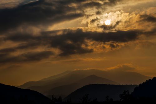 Free Peaceful mountain landscape at sunrise with clouds and sun backlighting the scene. Stock Photo