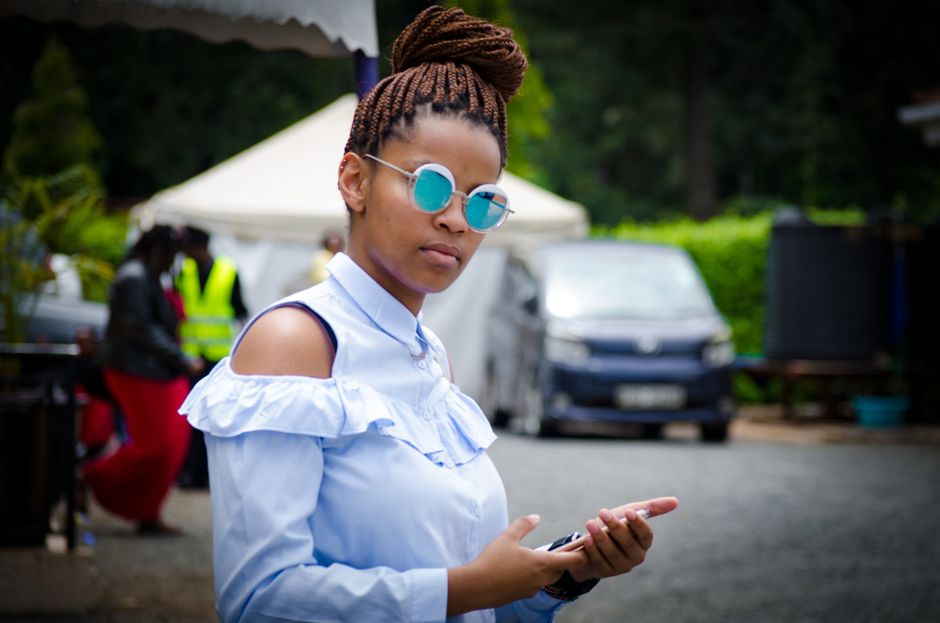 Stylish young woman wearing sunglasses and braided hair, holding a smartphone outdoors.