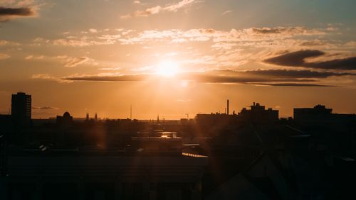 Free Silhouetted cityscape at sunset with stunning sunrays and clouds. Stock Photo