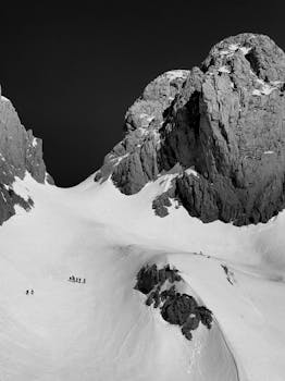 Black and white photo of snow-covered peaks in Qender Theth, Albania, with climbers in the foreground.
