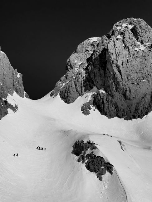 Black and white photo of snow-covered peaks in Qender Theth, Albania, with climbers in the foreground.