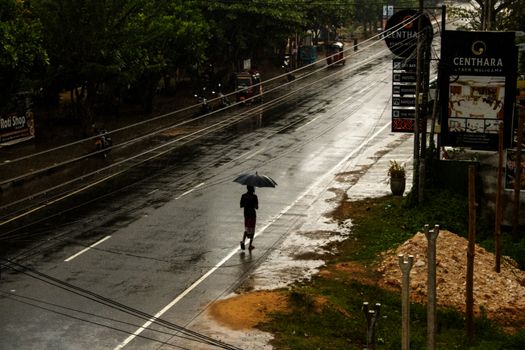 A person walks with an umbrella on a rainy day down an empty street, invoking solitude.