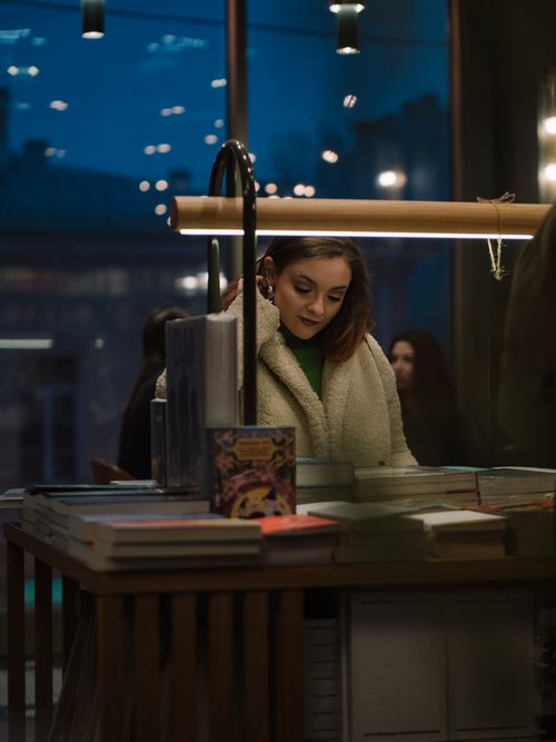 Free A woman in a cozy bookshop at night, surrounded by books under warm lighting. Stock Photo