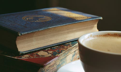 Book Beside Cup Filled With Brown Liquid