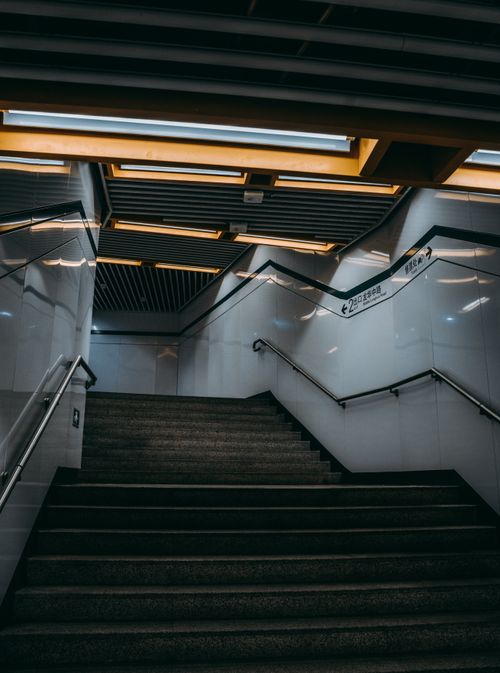 Free A low angle shot of a modern subway staircase featuring geometric ceiling lights and tiled walls. Stock Photo