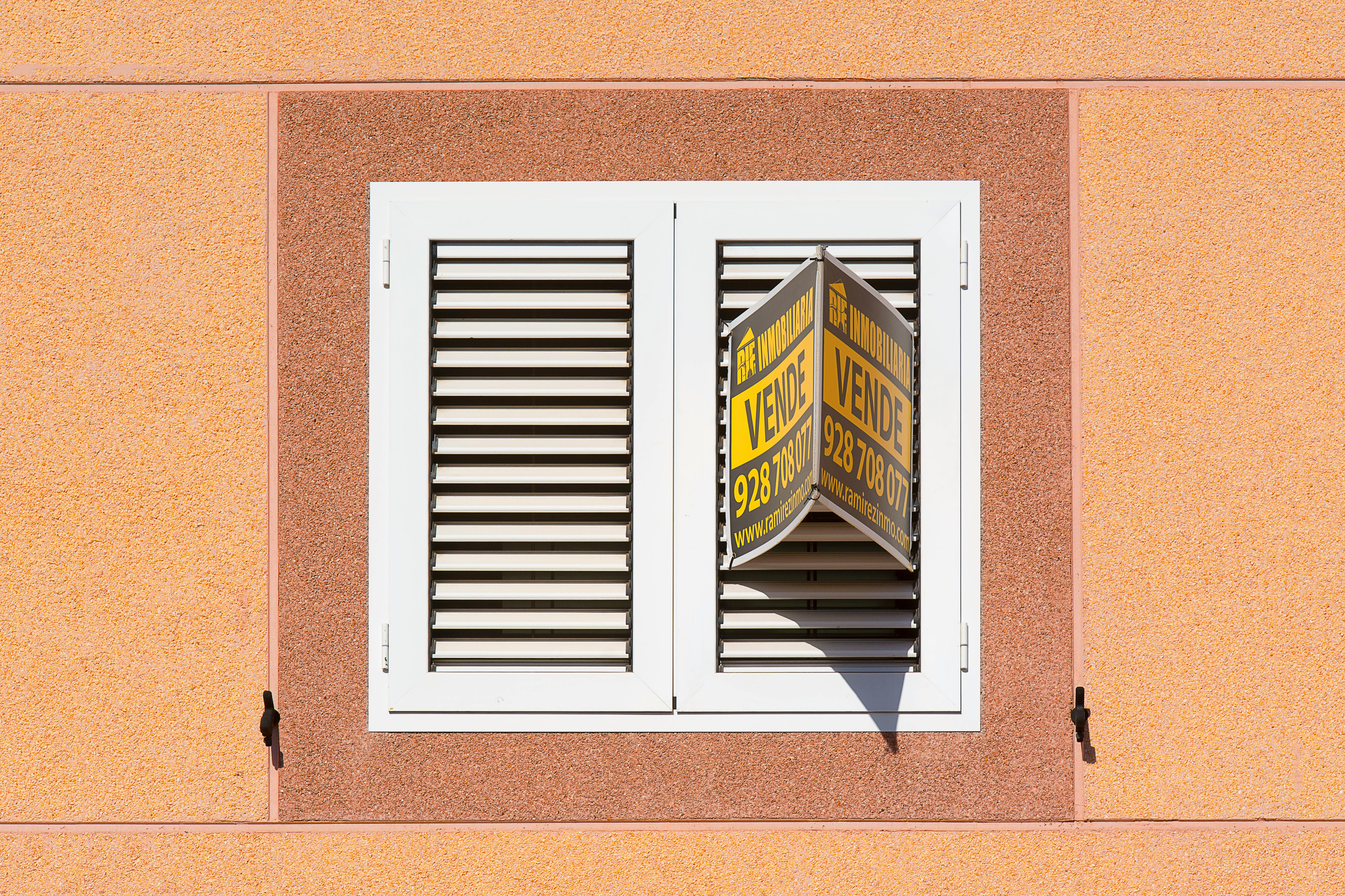 White shutter window with a for sale sign on peach building exterior.