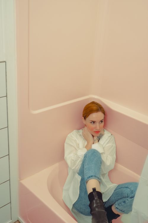 Free A stylish woman sitting in a pastel pink bathtub, exuding modern elegance. Stock Photo