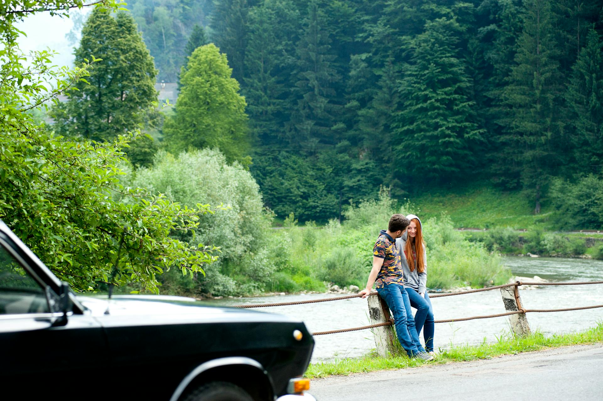 A young couple seated by a river enjoying a relaxing moment in a lush forest environment.