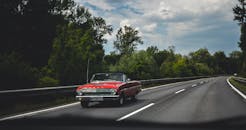 一辆复古红色敞篷车沿着风景优美、绿树成荫的高速公路行驶