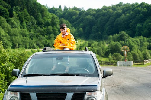 Child in Yellow Jacket Sitting on Roof of Nissan Frontier Through the Sunroof
