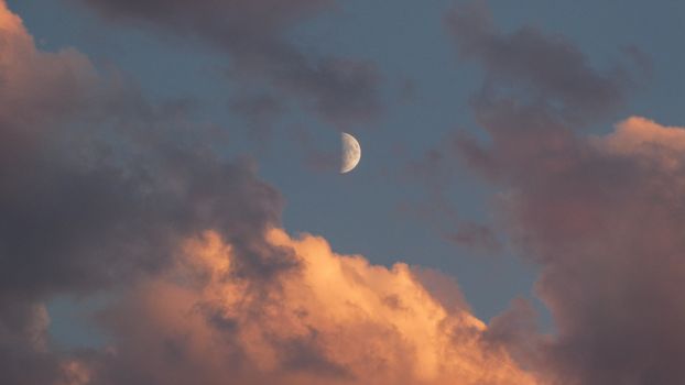 A serene view of the moon surrounded by colorful clouds in Canmore, Alberta.