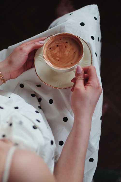 Free Aerial view of a woman holding coffee in a stylish polka dot dress, perfect for lifestyle and fashion themes. Stock Photo
