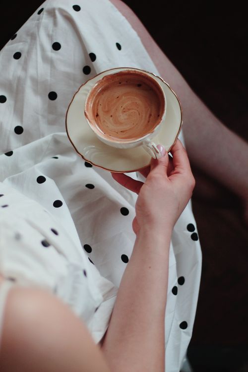 Free A woman in a polka dot dress holding a cup of black coffee, viewed from above. Stock Photo