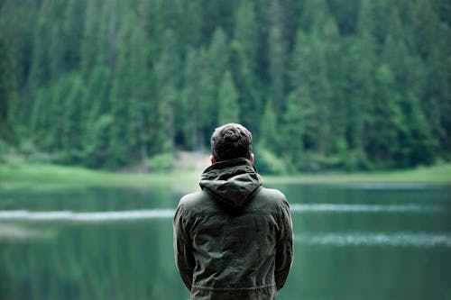 Free Photo of Man Wearing Hooded Jacket in Front of Body of Water Stock Photo