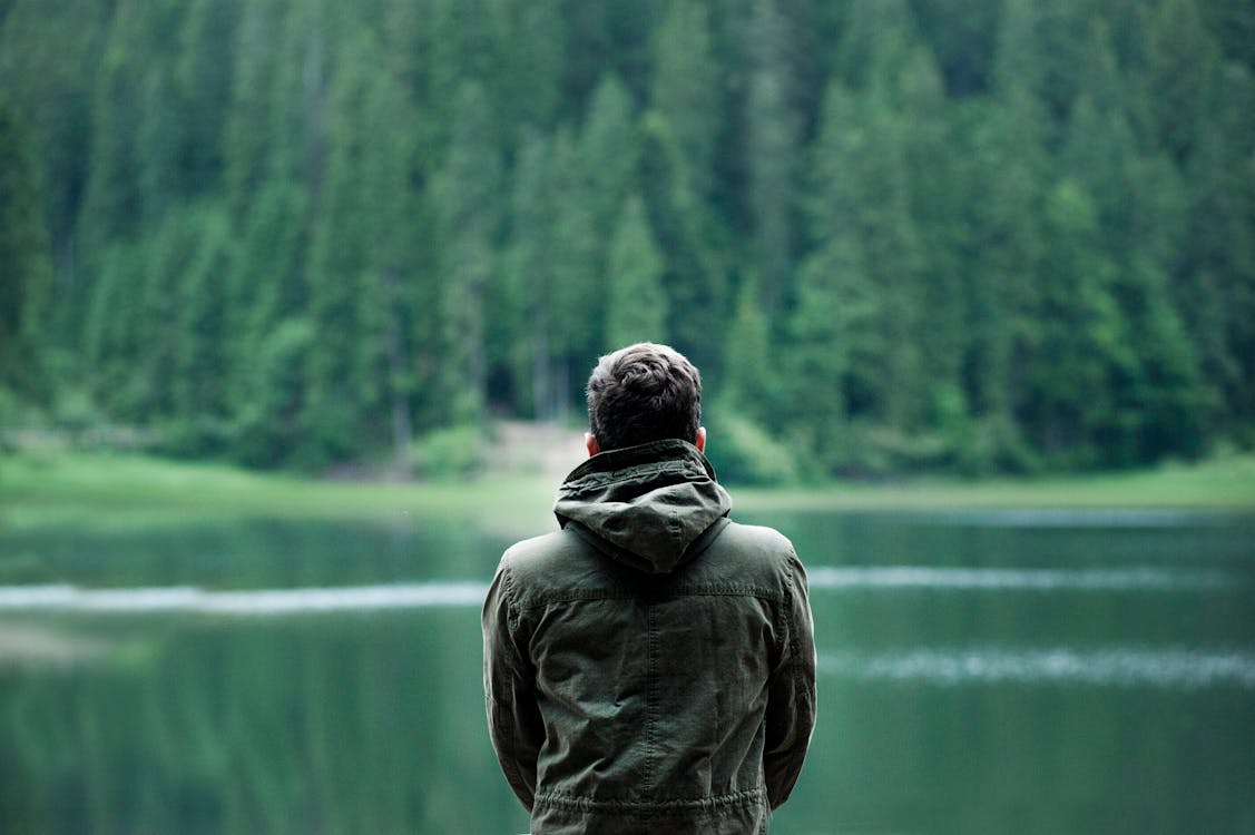 Photo of Man Wearing Hooded Jacket in Front of Body of Water