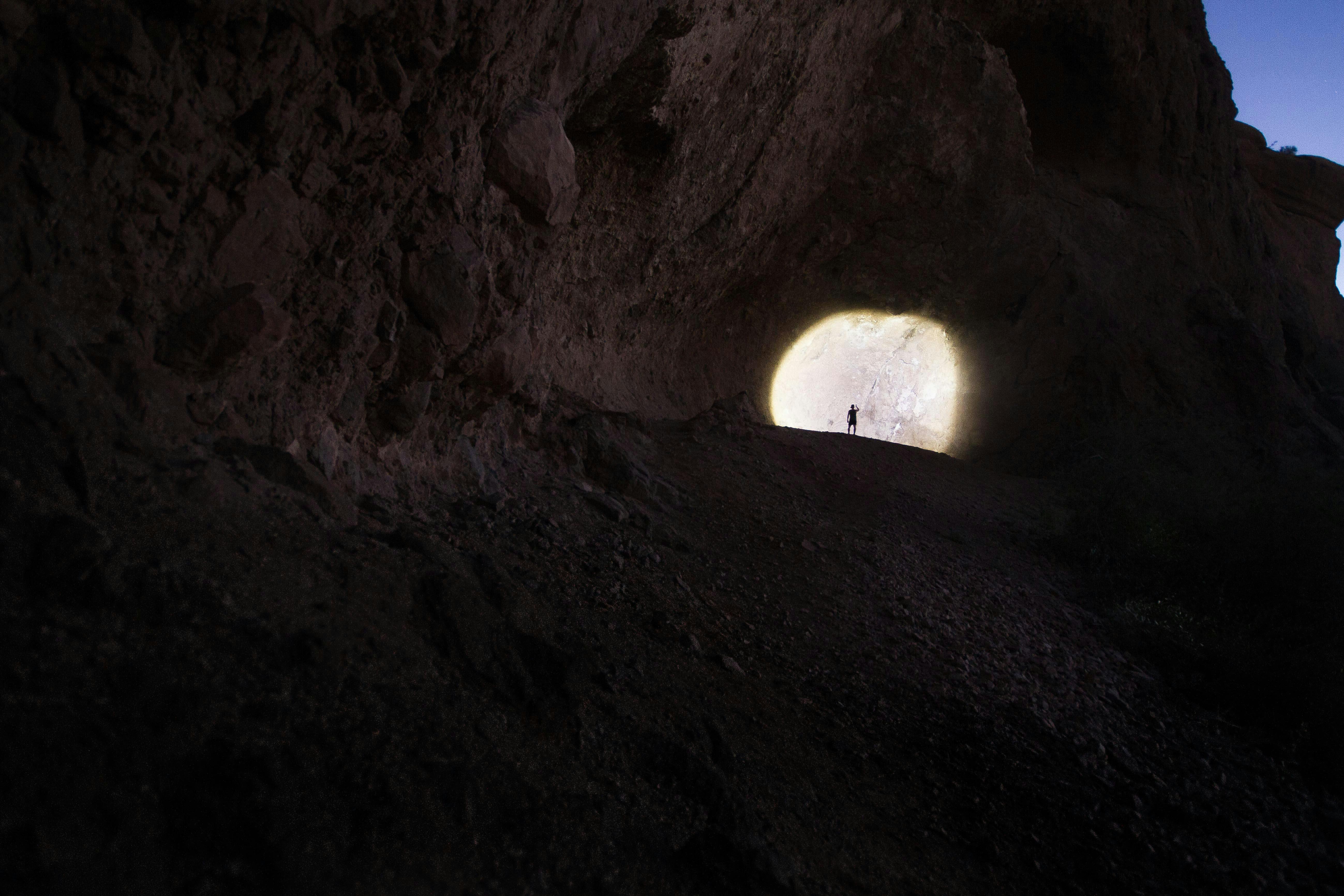 A solitary hiker stands silhouetted in a cave entrance at dawn, Scottsdale, AZ.