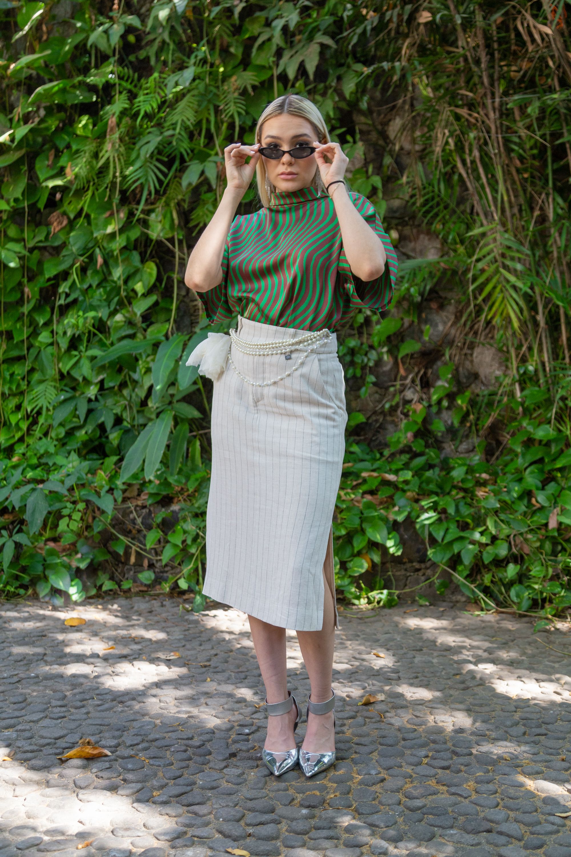 A fashionable woman poses confidently outdoors, showcasing a chic outfit and sunglasses.