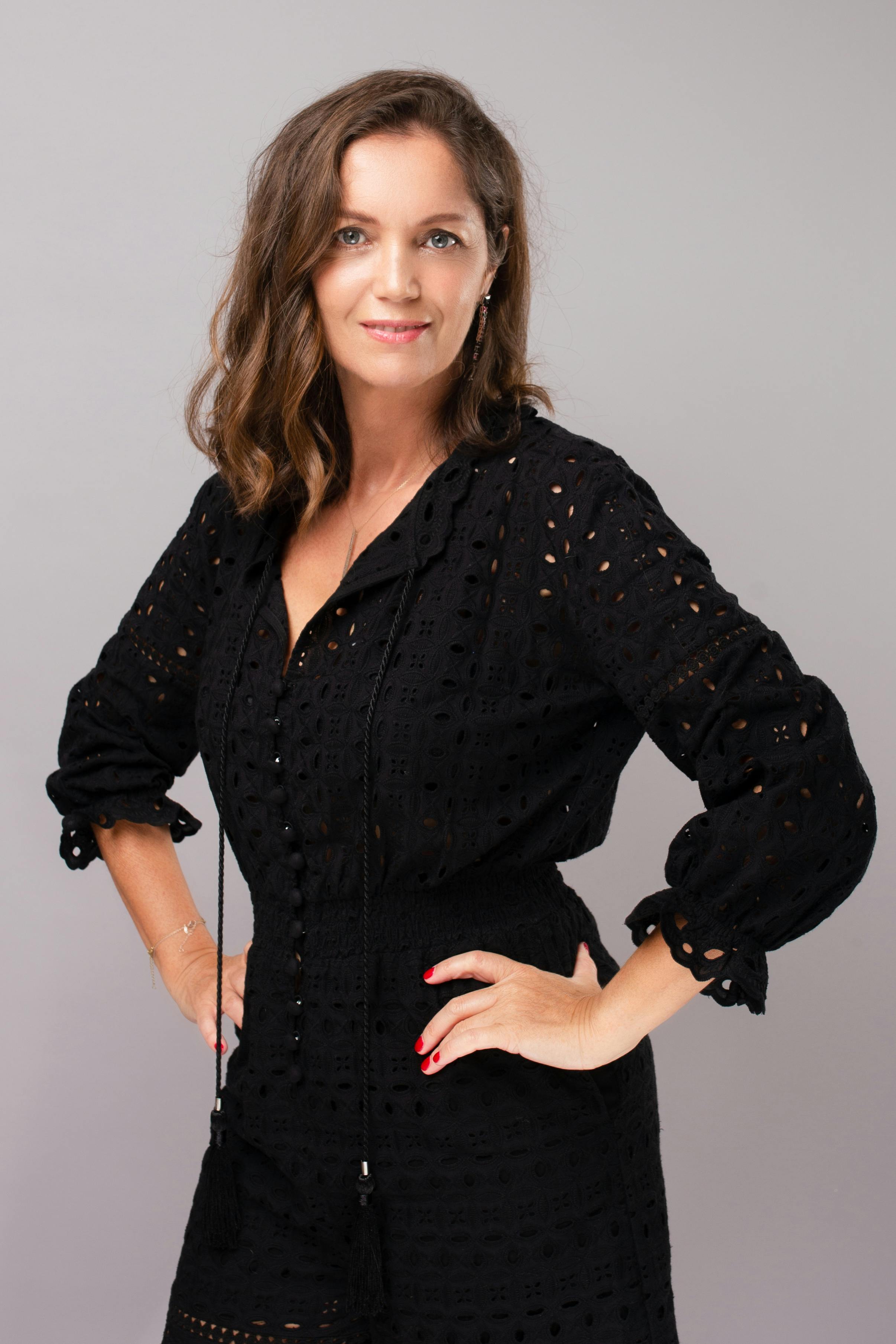 Portrait of an elegant woman posing confidently in a stylish black dress against a neutral background.