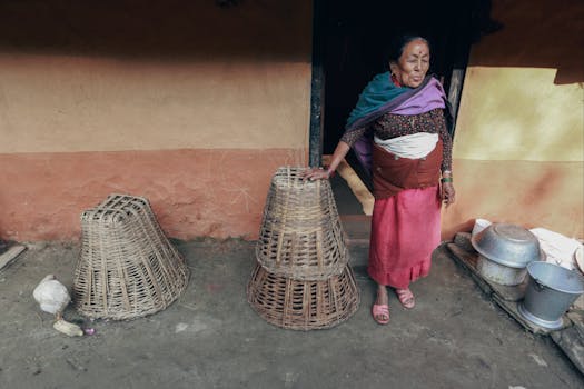 Elderly woman stands beside woven baskets in a rural setting, exuding traditional charm.