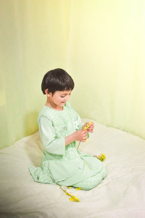 Girl in Dress Sitting on Bed while Holding a Flower