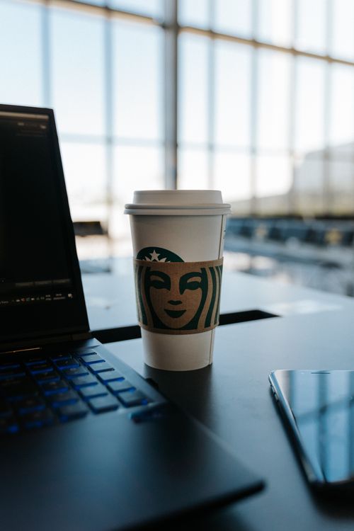 Free Disposable coffee cup on office table with laptop and phone nearby, in a bright workspace environment. Stock Photo