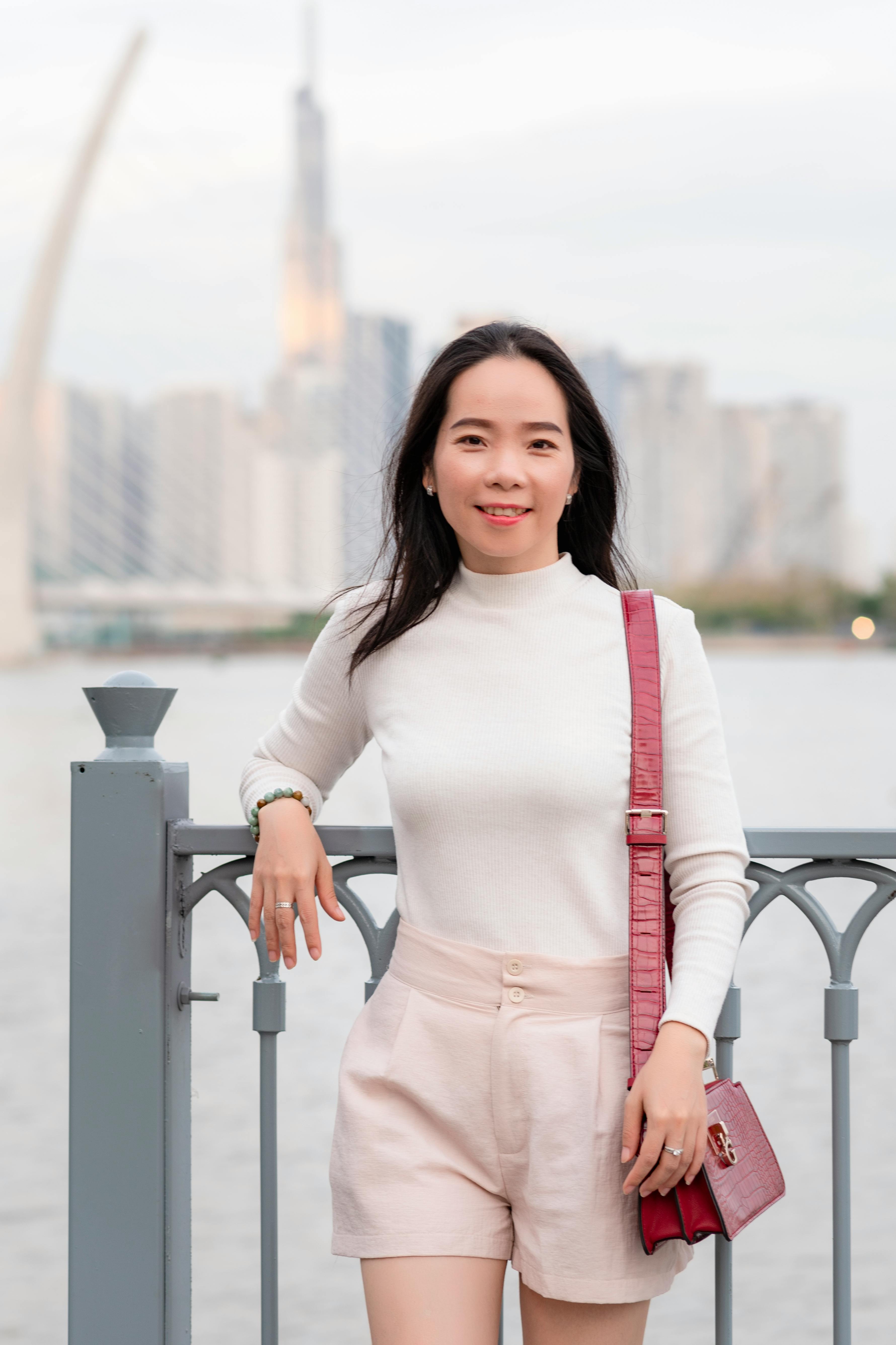 A smiling woman leaning on a railing with a blurred Ho Chi Minh City skyline in the background.