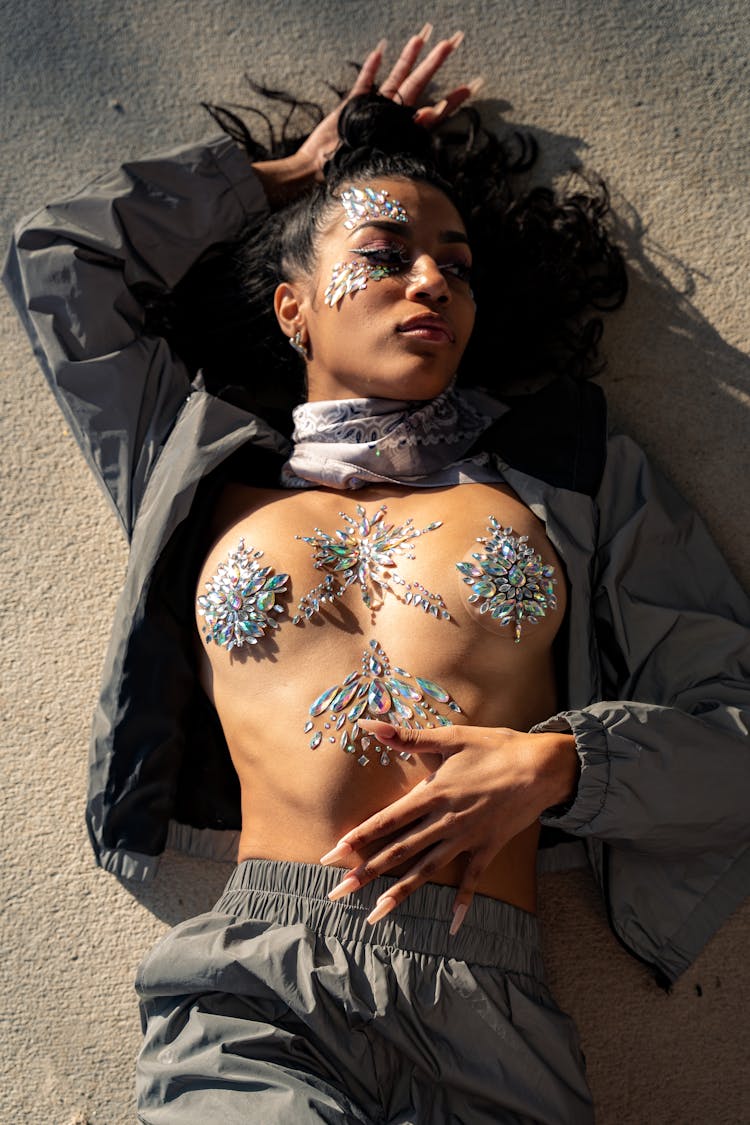 Shirtless Woman Lying On Ground With Crystals Decorating Her Face And Body