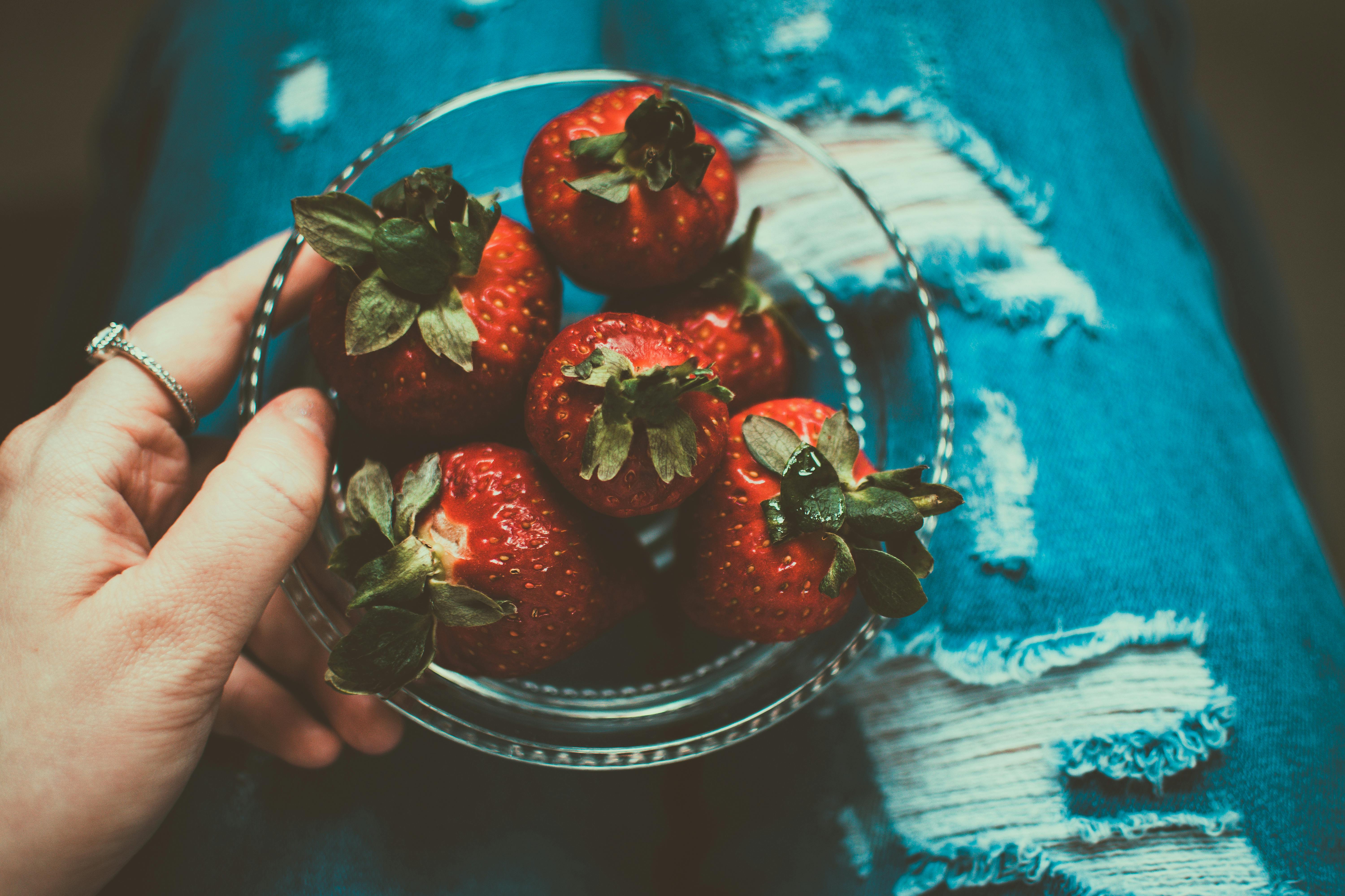 person holding clear glass bowl of strawberries